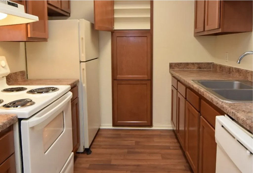 A kitchen with a white stove top oven, white dishwasher, and brown cabinets.